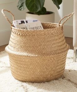 De COCO - lichte opbergmand van zeegras met twee handgrepen zit op een crèmekleurig tapijt en bergt tijdschriften op. Een plant en een deel van een beige sofa verschijnen op de achtergrond.