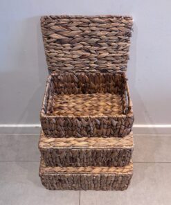 Drie SUNA kleine gevlochten opbergmanden van zeegras zijn gestapeld: het deksel van de bovenste mand is open en laat de binnenkant zien, terwijl de andere twee gesloten blijven. Ze zijn allemaal gemaakt van natuurlijk zeegras en staan tegen een lichte muur en tegelvloer.