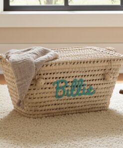 De PALM - rechthoekige opbergmand van palmblad ligt op een crèmekleurig tapijt, met een grijze deken over één kant gedrapeerd en de naam Billie in grote, groenblauwe letters geschreven.