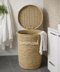 De RIVA - wasmand van palmblad met deksel staat open in een badkamer naast witte handdoeken, een plant en een witte kast, met kleding gedrapeerd over de rand.