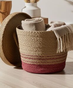 De RODO - ronde zeegras mand met deksel, met een roodroze basis, staat open op een lichte houten vloer met een beige handdoek en een deken met franjes erin. Op de achtergrond staan nog een mand en een vaas.