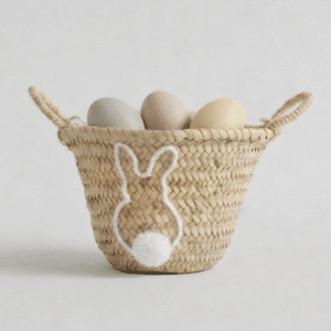 Het Paasmandje is een geweven mandje met een wit konijntje en een pomponstaart, gevuld met pastelkleurige eieren in groen, roze, geel en beige.